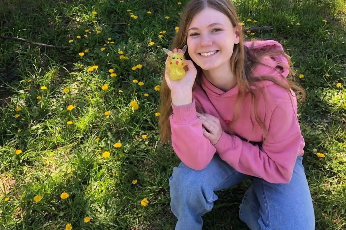 Isabelle smiling outdoors in a field of yellow flowers while holding a small yellow toy